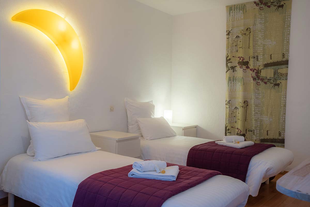 Single beds in hotel room with moon-shaped sconce near Saintes